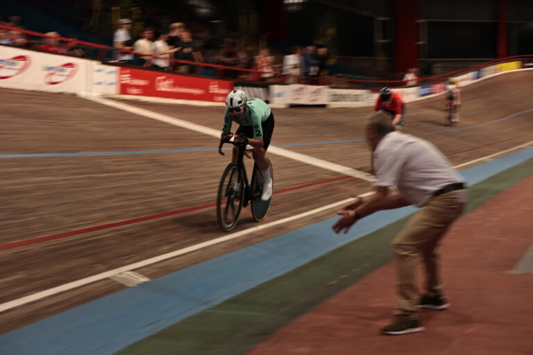 Radrennfahrer im Zielsprint auf der Bahn, Trainer beugt sich motivierend in Richtung Fahrer.