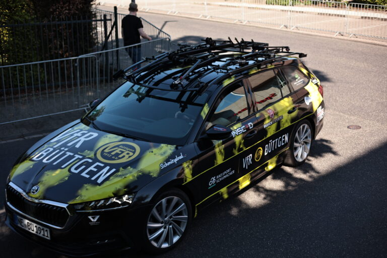 Teamfahrzeug des VfR Büttgen mit auffälligem Branding und Radträgern auf dem Dach, geparkt an einer gesperrten Straße.