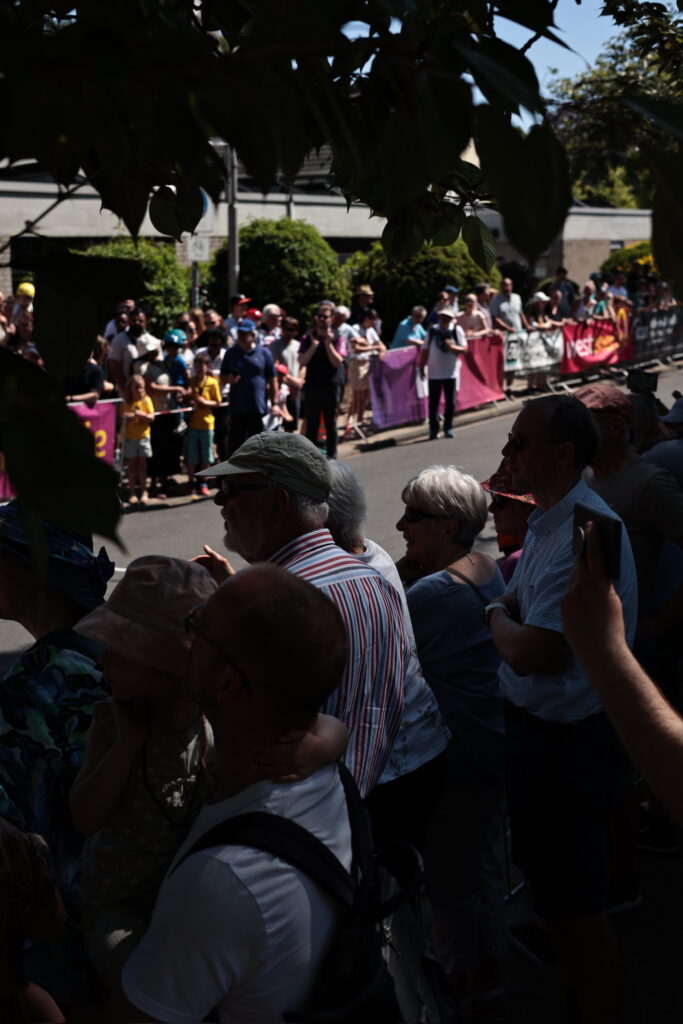 Publikum an einer abgesperrten Straße, gespanntes Warten auf das Renngeschehen, viele Menschen im Schatten.