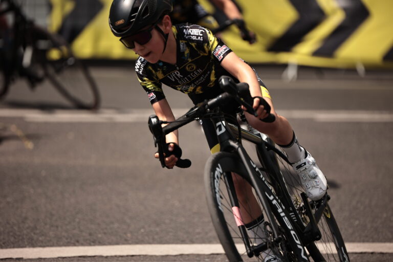 Kind im VfR Büttgen Trikot beim Straßenrennen in tiefer Kurvenlage, konzentriert nach vorn blickend.