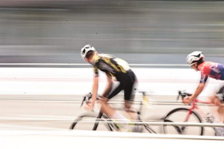 Bewegungsunscharfe Aufnahme von zwei Radsportlern im Renntempo, einer im VfR Büttgen Trikot, einer in rotem Trikot.