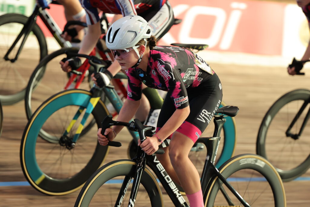 Radrennfahrerin in pink-schwarzem VfR Büttgen Trikot bei einem Bahnrennen in tiefer Fahrposition.